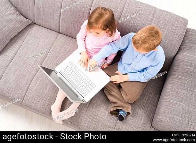 Overhead shot of children sitting on couch at home, using laptop computer, looking at screen