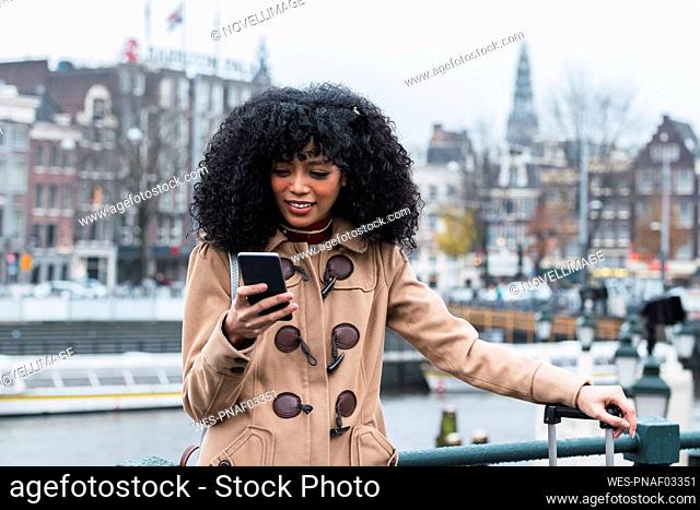 Young woman with curly hair using smart phone in city