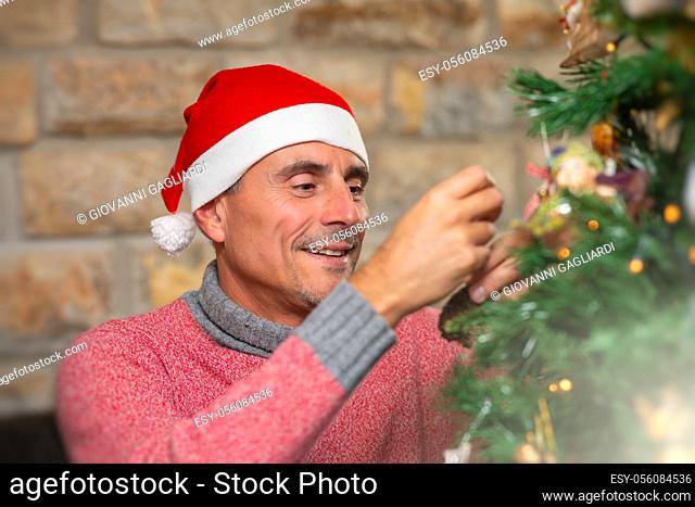 Man wearing Christmas Hat at home decorating Christmas Tree