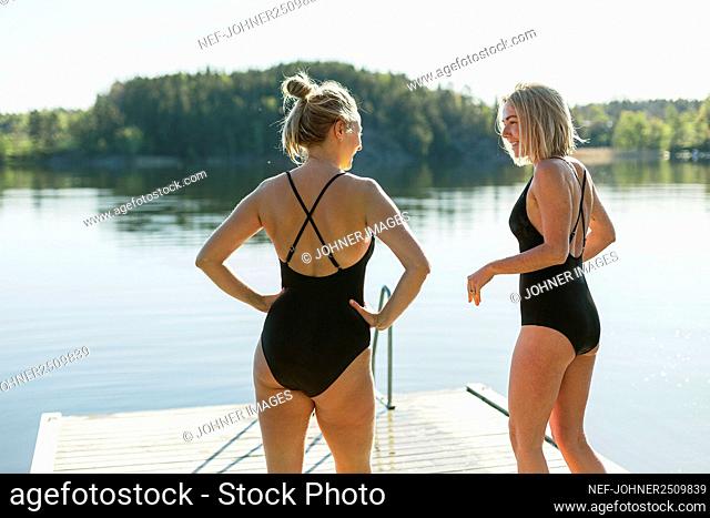 Women in swimsuits standing on deck at lake