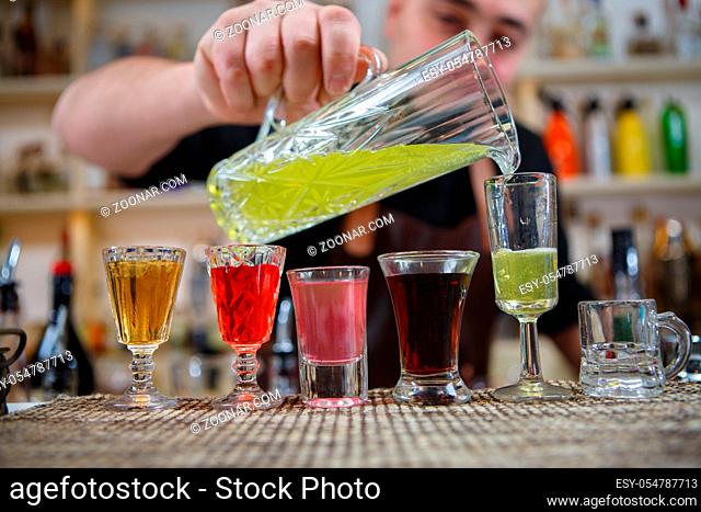 Bartender pours various of alcohol drink into small glasses on bar