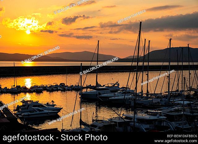 Alghero, Sardinia / Italy - 2018/08/10: Summer sunset skyline over the Alghero Marina yacht port at the Gulf of Alghero at Mediterranean Sea