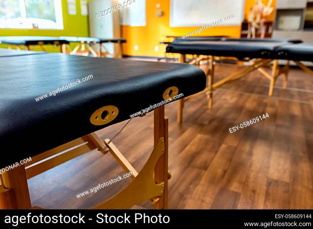 A close up view on the end of a massage table with leather cushions and brass slots for headrest, many empty beds are seen in the background with copy space