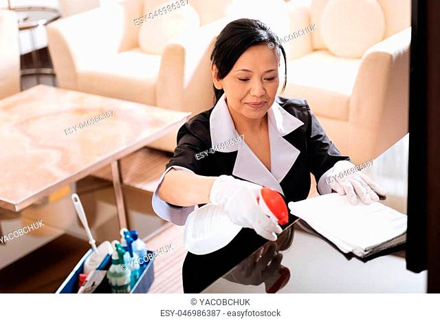 Perfect shine. Nice pleasant joyful woman holding a cleansing agent and spraying it on the table while doing the cleaning