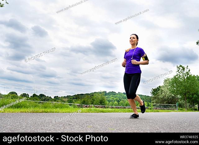 Urban sports - Woman running for better fitness in the city park on a cloudy summer day