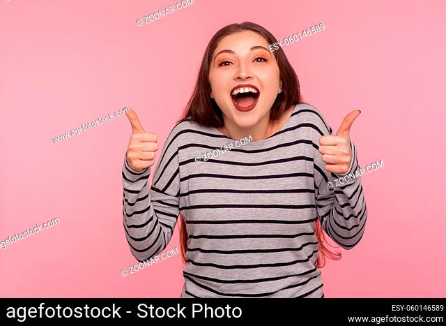 Excellent job, I like it. Portrait of overjoyed excited woman in striped sweatshirt doing thumbs up and shouting in happiness, satisfied with awesome result