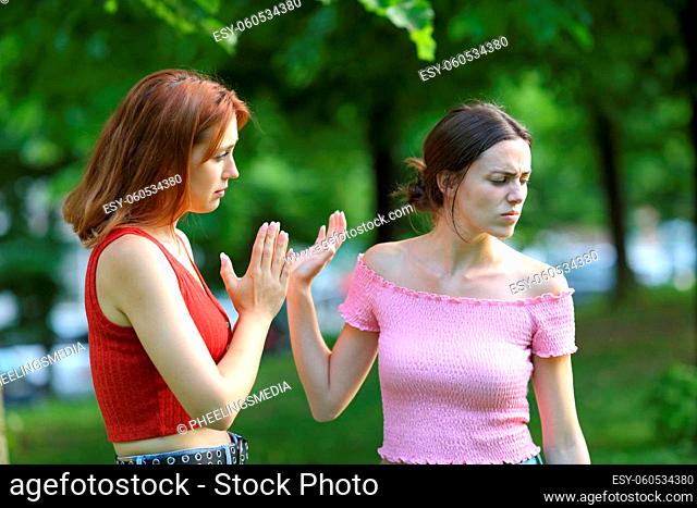 Regretful woman asking forgiveness to her friend in a park