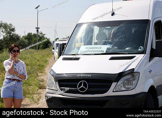 RUSSIA, KHERSON REGION - JUNE 23, 2023: A woman stands next to a shuttle bus as vehicles queue to pass the Armyansk checkpoint between the Kherson Region and...