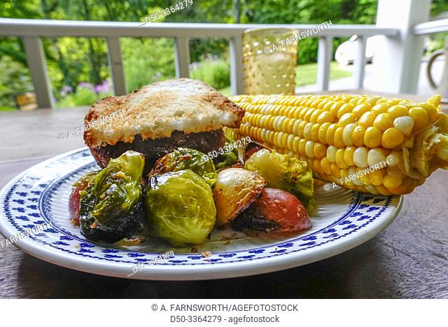 Cornwall, Connectcut, USA A plate of grilled potatoes and brussel sprouts with corn on the cob and an Impossible vegetarian burger