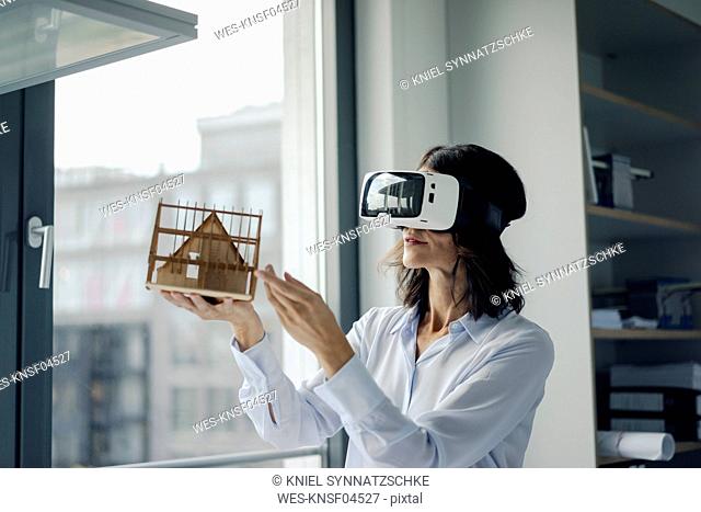 Woman holding architectural model of house, using VR glasses