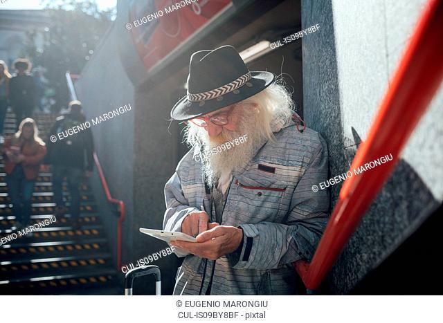 Senior man using digital tablet at entrance to subway, Milano, Lombardia, Italy