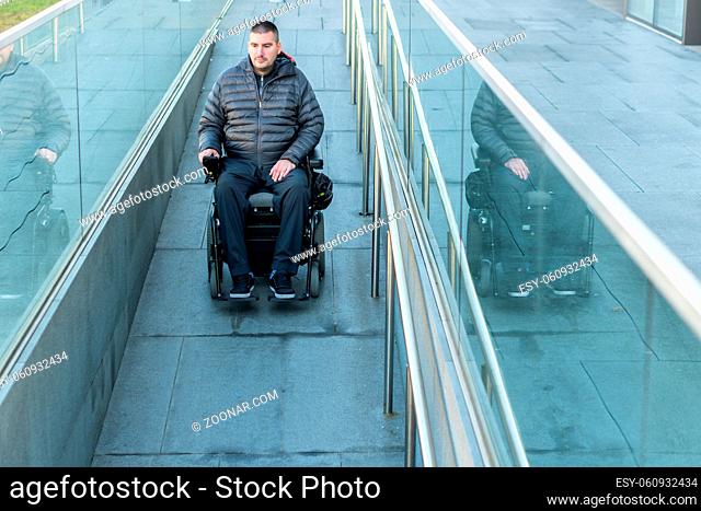 Man in a wheelchair using a ramp next to stairs