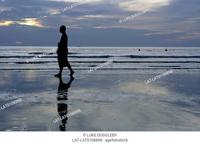 National park. Beach. Thai Buddhist monk in long robe. Walking on sand. Sunset. Low light. Silhouette