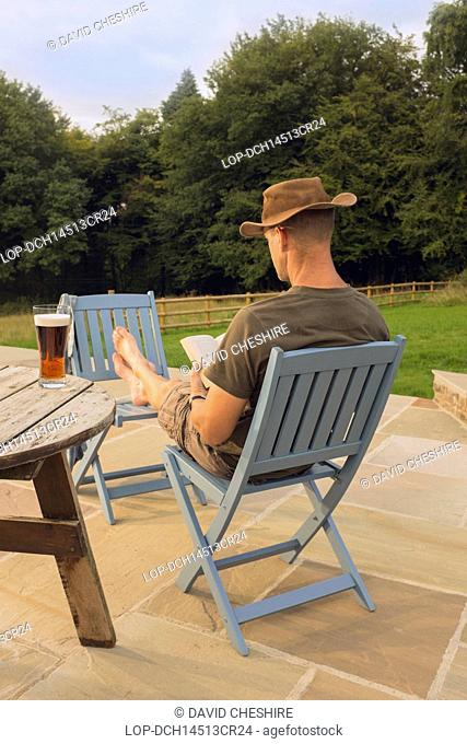 Wales, Monmouthshire, Monmouth. A man relaxing with a book and glass of beer
