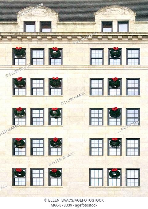 Many Christmas wreaths hanging from rows of windows on several floors of a white stone city building in New York City
