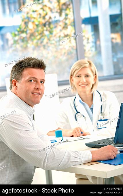 Doctor and patient sitting in office, looking at camera, smiling