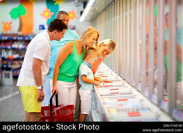 Young family shopping with the Grandparents in a supermarket standing with their young son at a food counter choosing produce