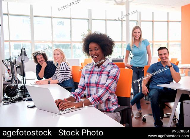 young smiling African American informal businesswoman working in the office with colleagues in the background