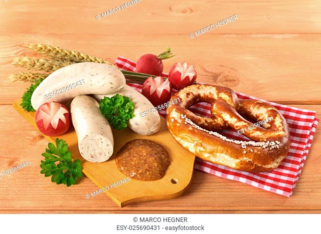 weißwurstfrühstück with sausages, pretzels and sweet mustard on wooden board\n