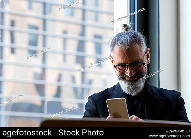 Smiling male entrepreneur working on mobile phone in coffee shop