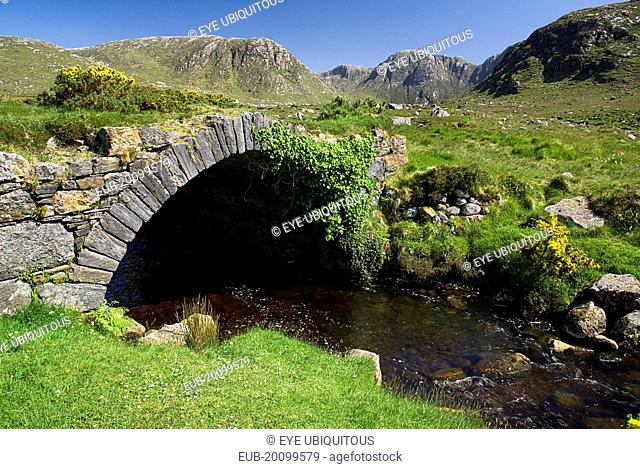 A stream runs under an old style stone bridge with the Derryveagh Mountain behind