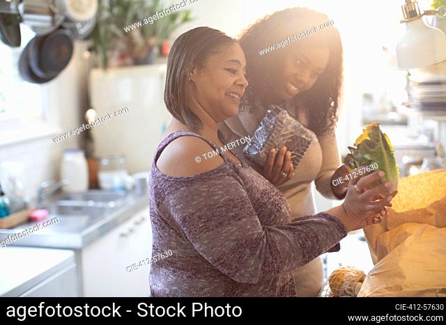 Mother and daughter unloading groceries in sunny kitchen