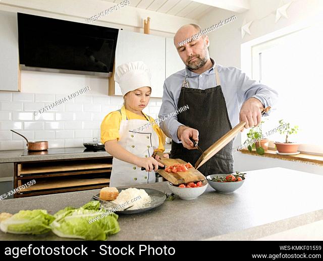 Daughter and father preparing food while standing together in kitchen at home