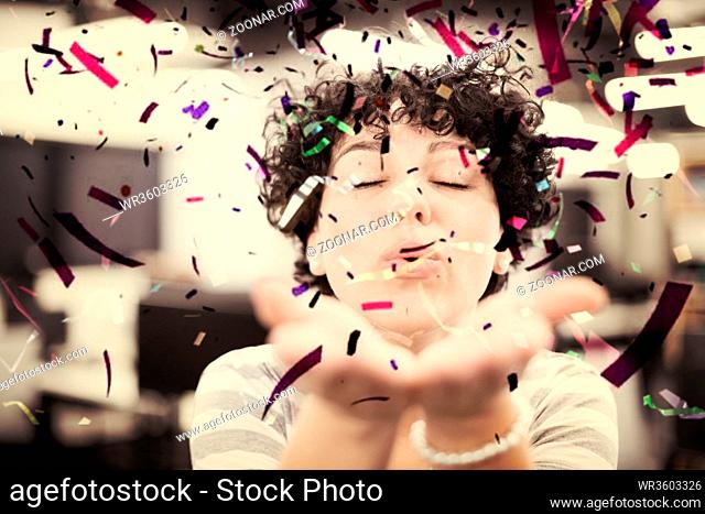 young female software developer having fun blowing confetti while celebrating new year at modern startup office