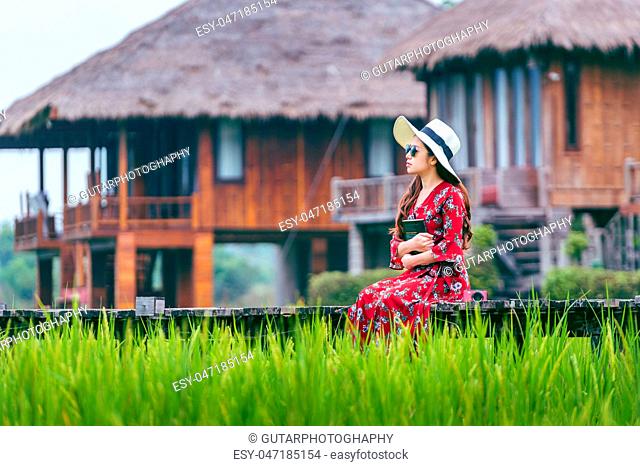 Young woman sitting on wooden path with green rice field in Vang Vieng, Laos