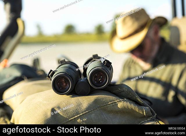 Binoculars on the dash of a safari jeep, a safari guide in the background