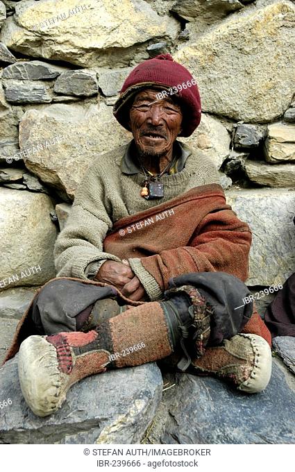 Old man wearing woolen cap and boots made of yak leather at a wall of stones Phu Nar-Phu Annapurna Region Nepal