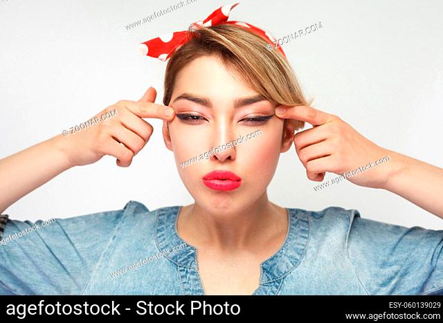 Portrait of blindness beautiful young woman in casual blue denim shirt with makeup and red headband standing, stretches eyes, try to see better