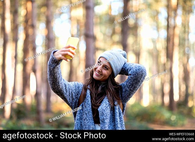 Smiling woman with hand behind head taking selfie while standing in Cannock Chase woodland