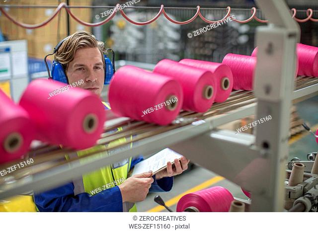 Man wearing ear defenders working at spool machine in factory