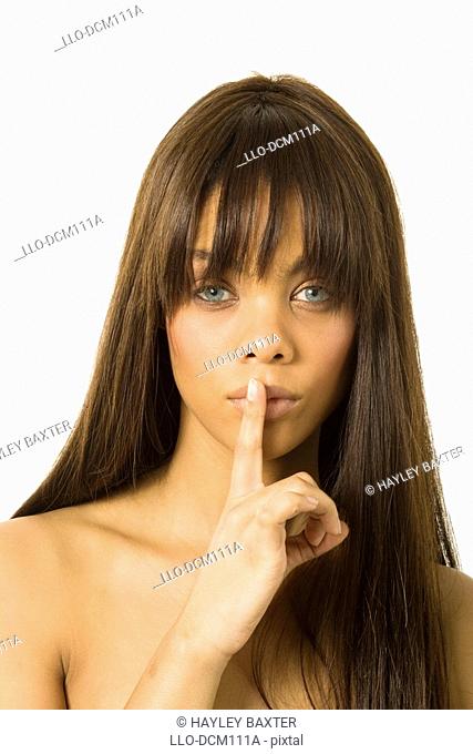 Studio shot of Young girl holding finger over mouth gesturing silence