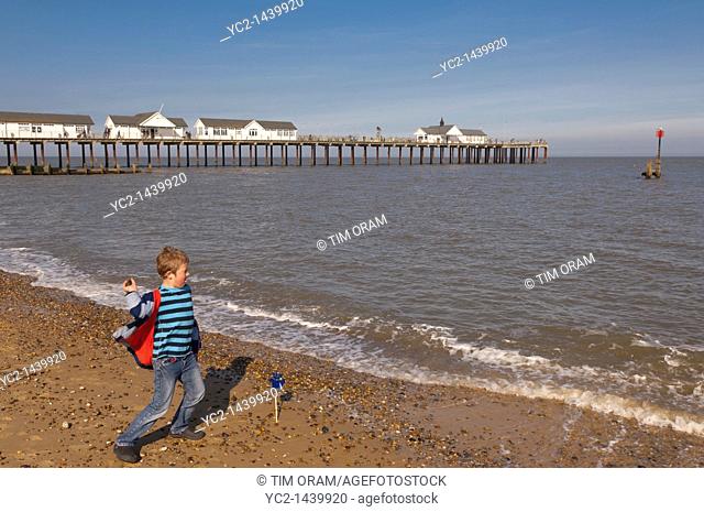 A seven year old boy throwing stones into the sea near the pier at Southwold , Suffolk , England , Britain , Uk