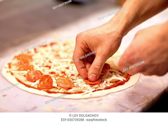 food, culinary, italian cuisine, people and cooking concept - cook hands adding salami slices to pizza at pizzeria