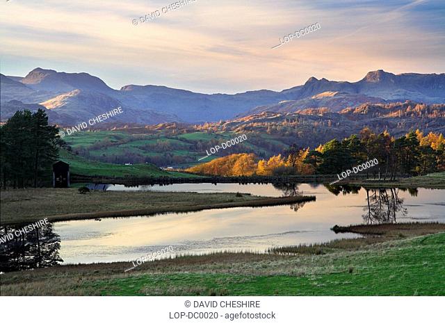 England, Cumbria, Conniston, Wise Een Tarn looks serene as the low evening sun catches the Langdale Pikes