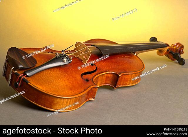 An old violin with slight scratches and damage lies on a neutral, gray, yellow-lit background. | usage worldwide. - /Deutschland