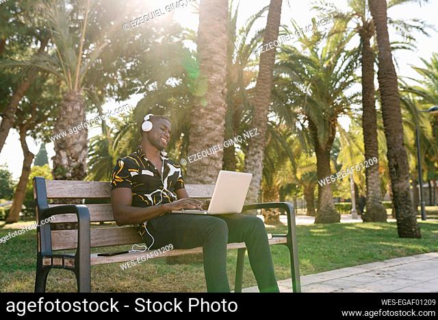 Male entrepreneur listening music while working on laptop in park