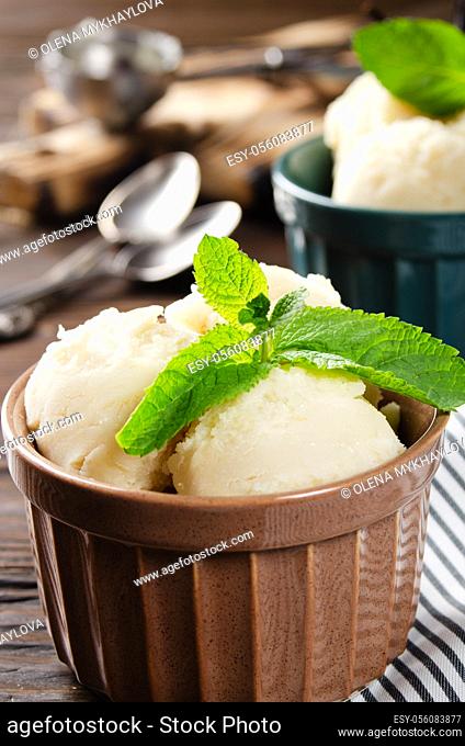 Vanilla icecream balls in clay bowls on wooden kitchen table with ice cream scoop aside