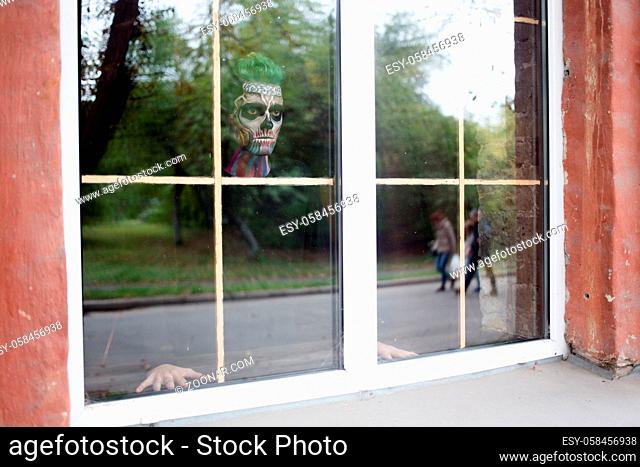 View of man with skeleton make up in the window. Halloween makeup concept, scary man in window