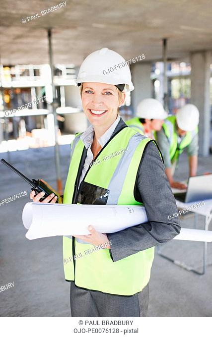 Construction worker holding walkie talkie and blueprints on construction site
