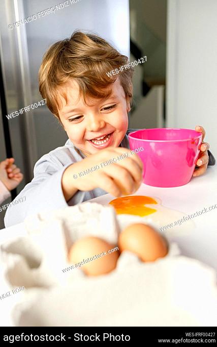 Mischievous boy breaking egg yolk on table in kitchen