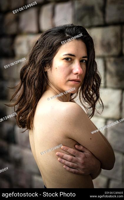 Portrait of a 27 year old white woman with folded arms, showing her naked back and torso, Brussels, Belgium