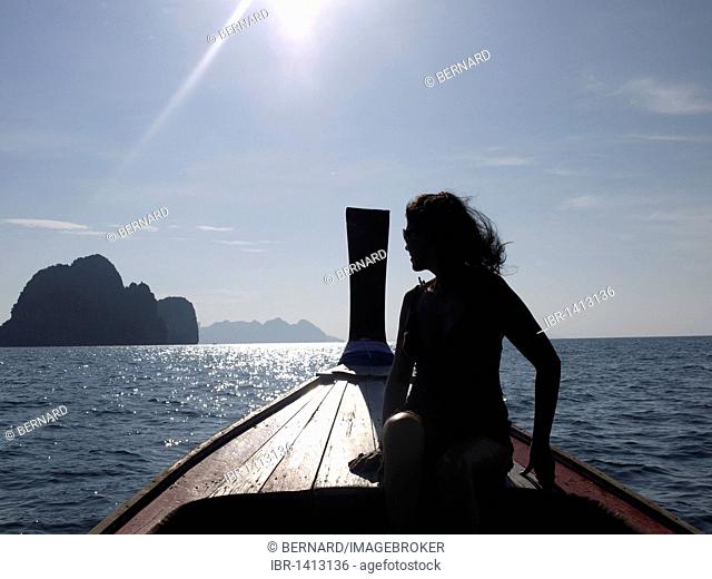 Woman in the back on a long tail boat, sitting in front of a group of rocks and Ko Muk island, seen from the direction of Ko Hai island, Ko Ngai, Andaman Sea