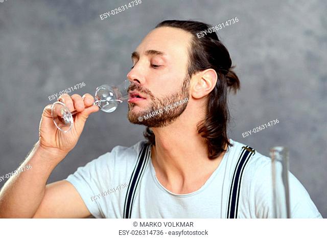 young man in front of gray background drinking clear spirit
