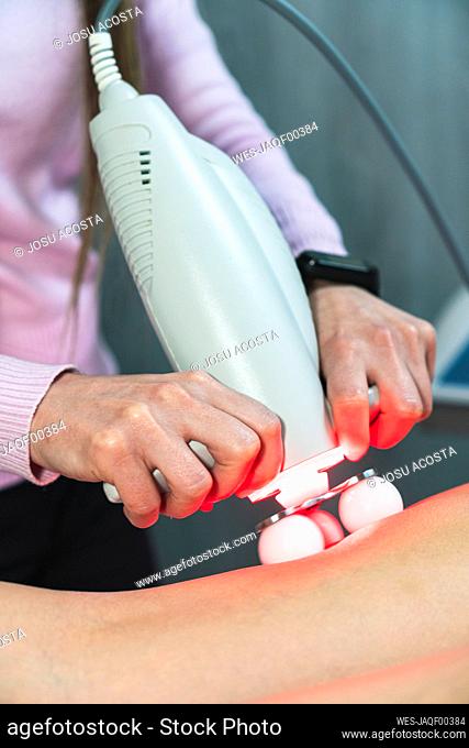 Hands of female aesthetician massaging legs of young woman with laser massager