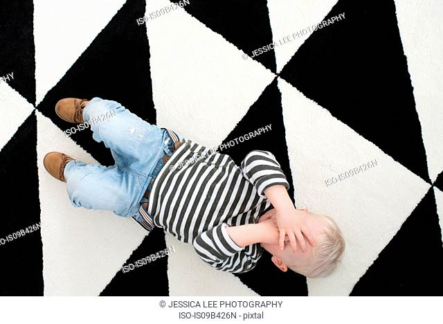 Young boy lying on floor, covering eyes, elevated view