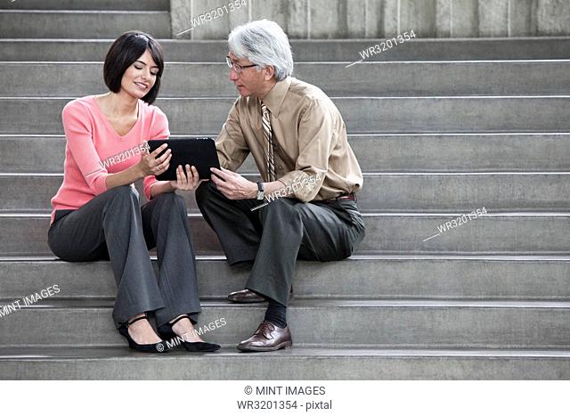 Hispanic businesswoman and Asian businessman working on a notebook computer while sitting on the steps of a convention centre